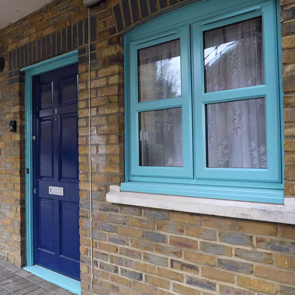 A detailed view of external property services, showing a freshly painted dark blue front door and a matching turquoise window set into a brick wall.