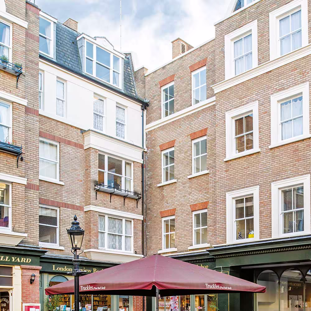 Looking up at the beautifully redecorated brick buildings of a London courtyard, with clean white window frames and architectural details.