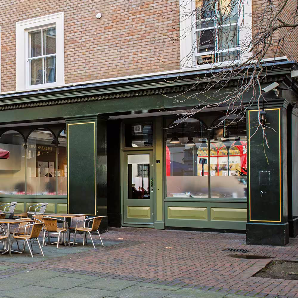 A newly redecorated dark green shopfront with gold trim and outdoor seating in a historic courtyard, reflecting the high quality of the external works.