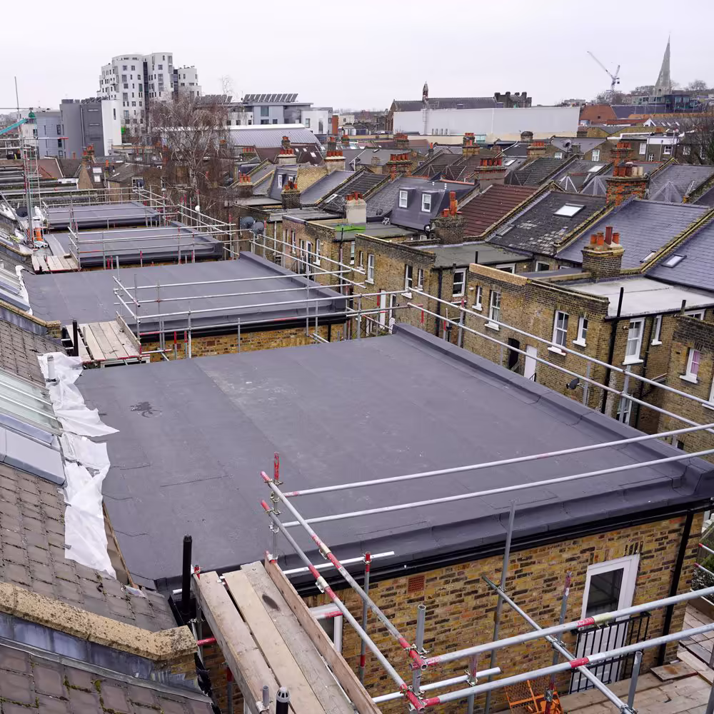 High-level look across scaffolded roofs as teams replace coverings and upgrade rainwater goods.