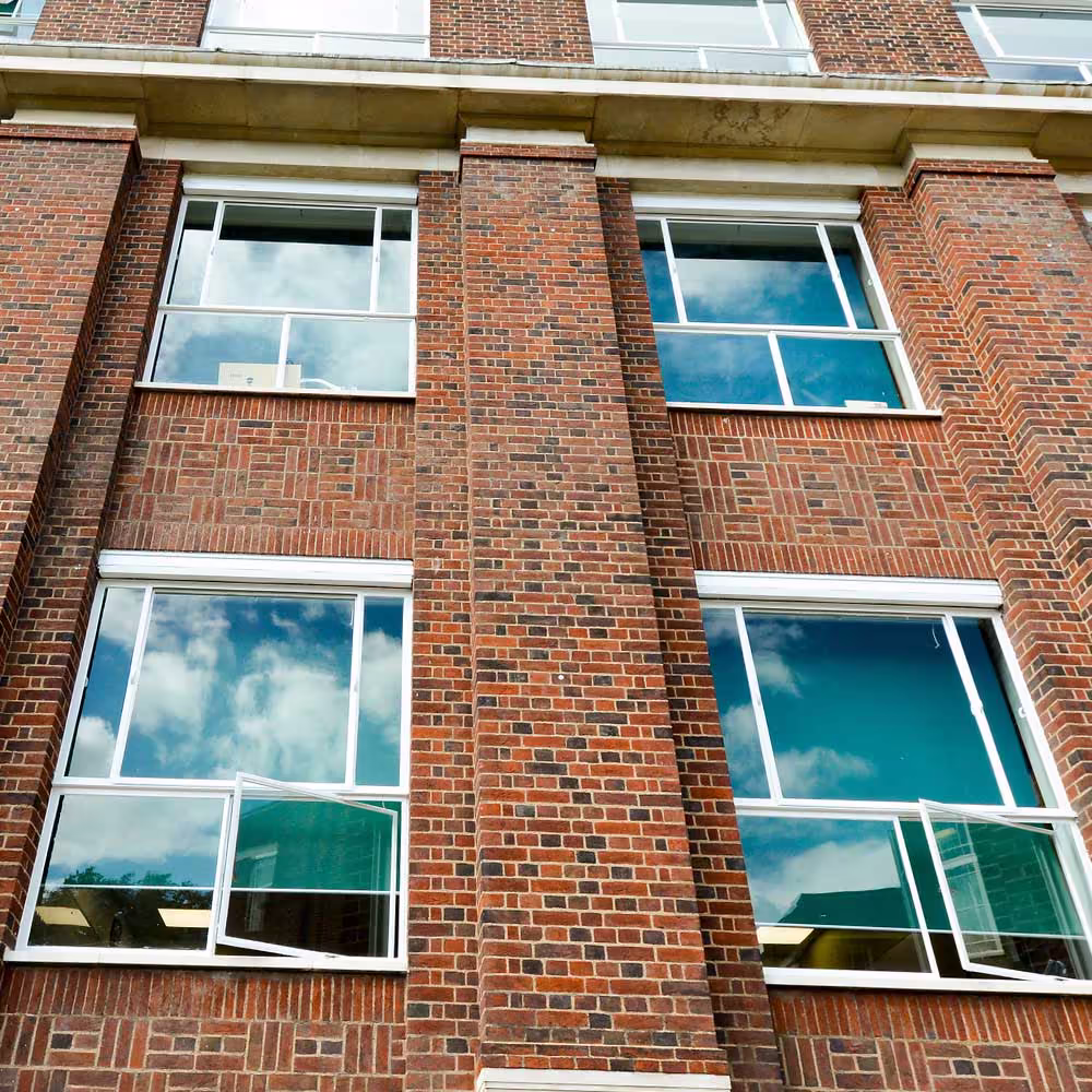 Close-up of the glazed facade reflecting blue sky, highlighting the renewed window frames and mastic seals.