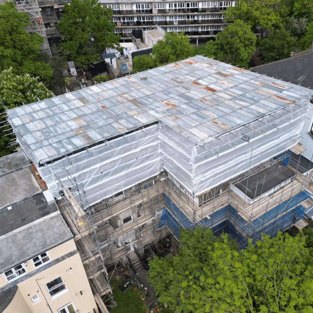 Aerial view of a large residential block undergoing extensive renovations, completely enclosed in protective scaffolding with a temporary roof.