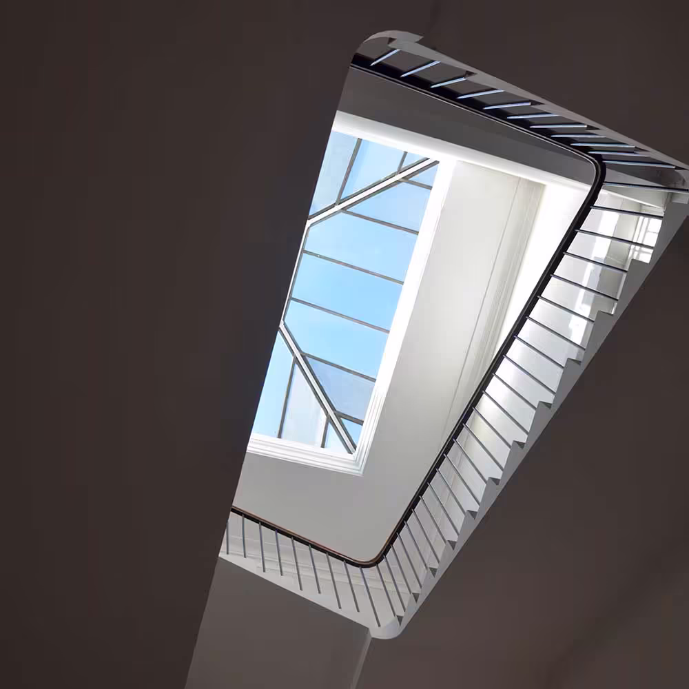 Looking up the stairwell of a Grade Listed building towards a large, modern skylight that floods the repaired and redecorated space with natural light.