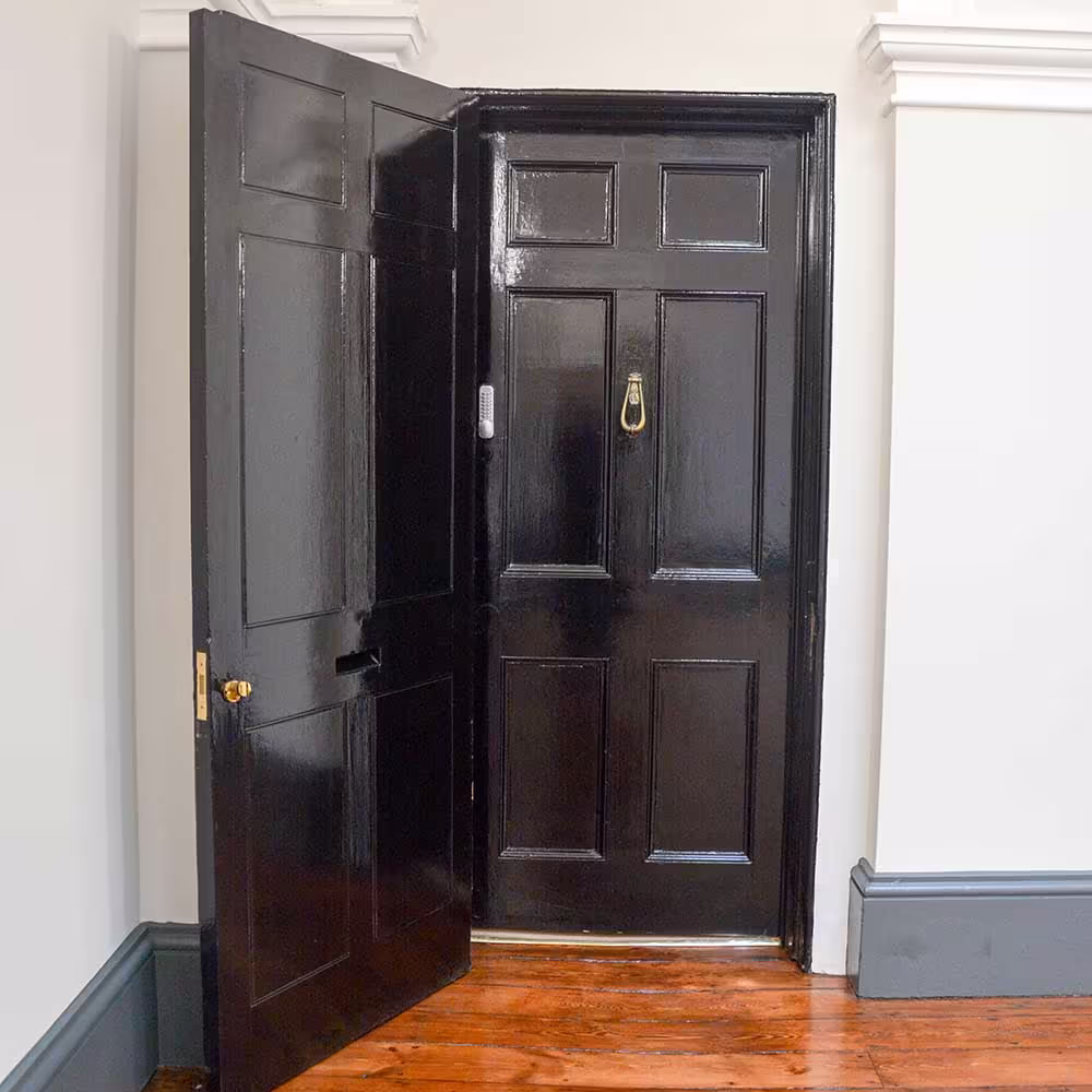 A traditional six-panel door in a Grade Listed property, expertly repaired and painted in a high-gloss black finish as part of the restoration project.