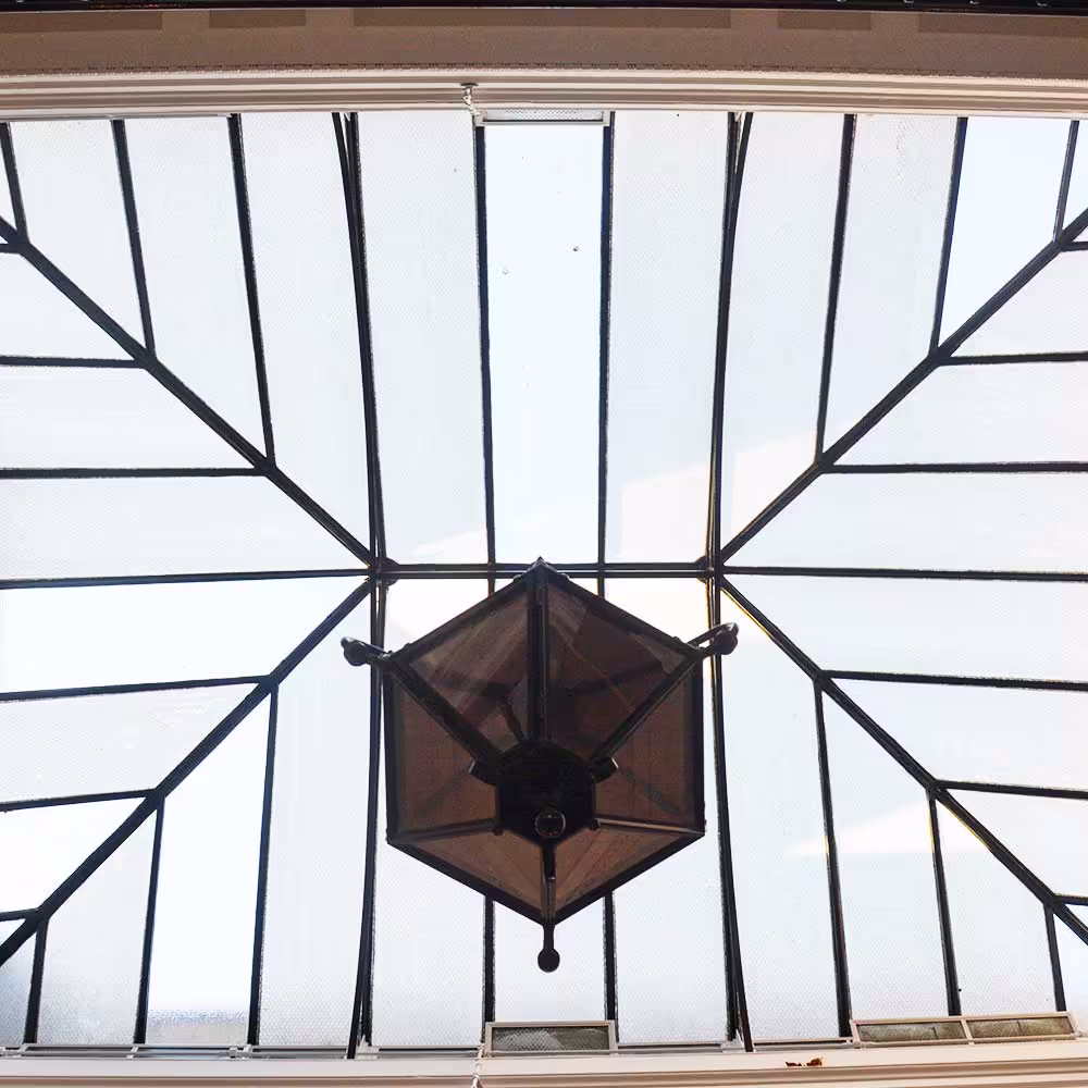 Looking up at a restored glazed atrium in a Grade Listed building, with a traditional hanging lantern suspended from the centre of the geometric leaded glass.