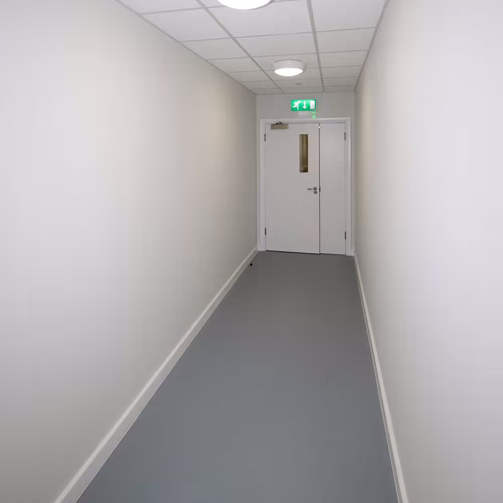 A clean, newly renovated corridor with white walls, grey flooring, and fire doors at the far end, part of a gymnasium renovation project.