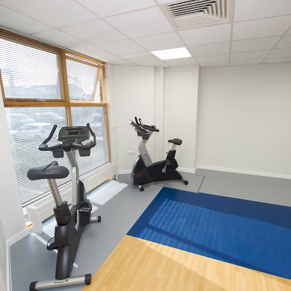 The cardio area of the renovated gym, featuring two exercise bikes by a large window and new multi-toned safety flooring.