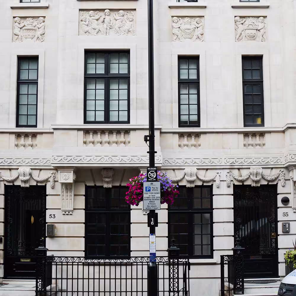 The impressive stone facade of a conserved heritage building on a London street, showing ornate stone carvings, grand entrances, and restored black iron railings.