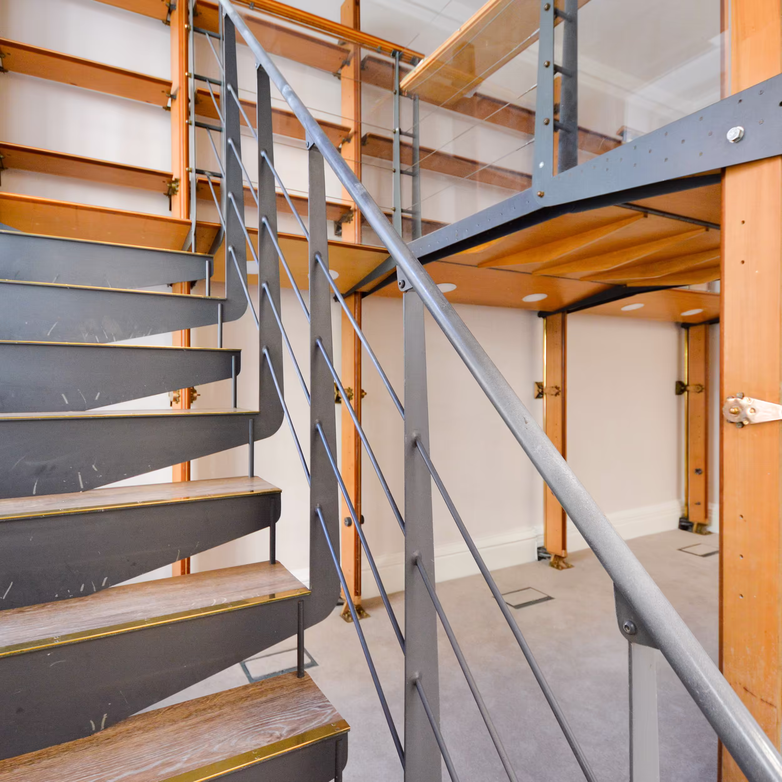 A modern, industrial-style steel and wood staircase installed within a renovated heritage building, leading up to a mezzanine level with library shelving.