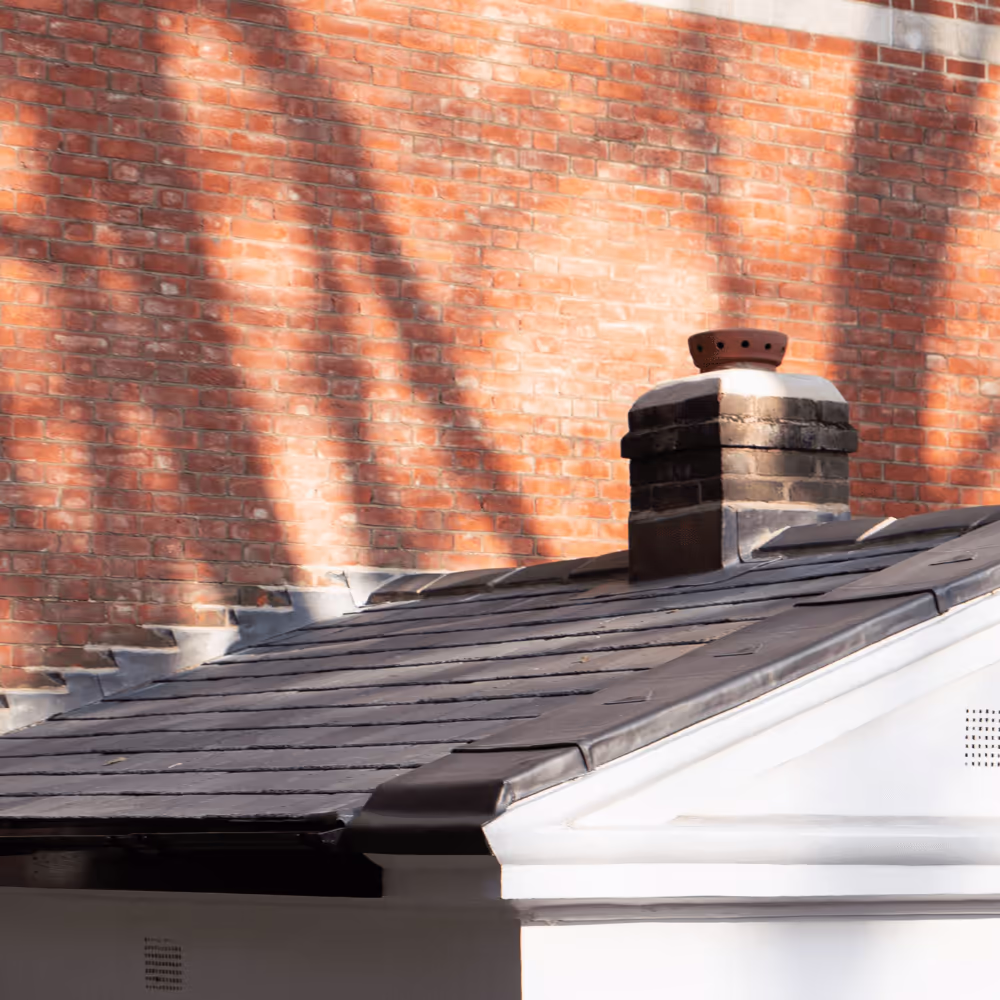 Detail of the high-quality heritage roofing, showing the new dark slate tiles and a restored brick chimney pot against a sunlit brick wall.