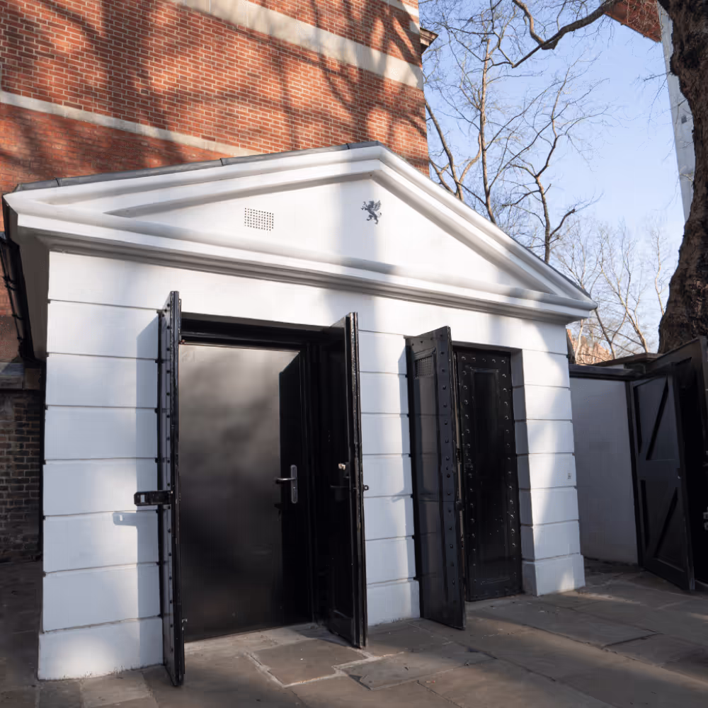 The restored white classical-style gatehouse, a heritage conversion project, featuring its distinctive pediment and robust new black security doors.