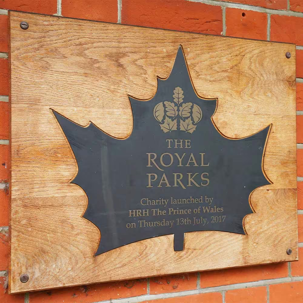 A close-up of the wooden plaque for 'The Royal Parks' charity, commemorating its launch by HRH The Prince of Wales in 2017.