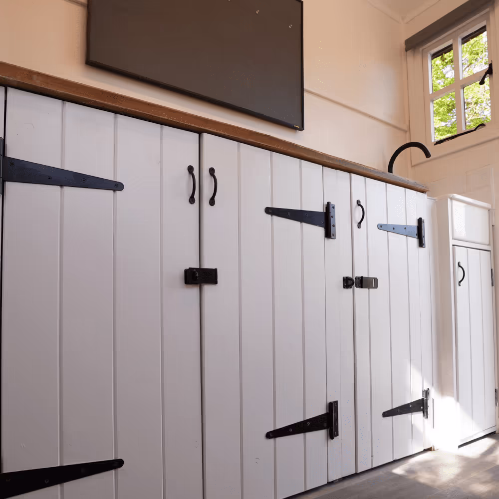The interior of a refurbished heritage park building, showing custom-built white cupboards with traditional black wrought iron hinges and handles.