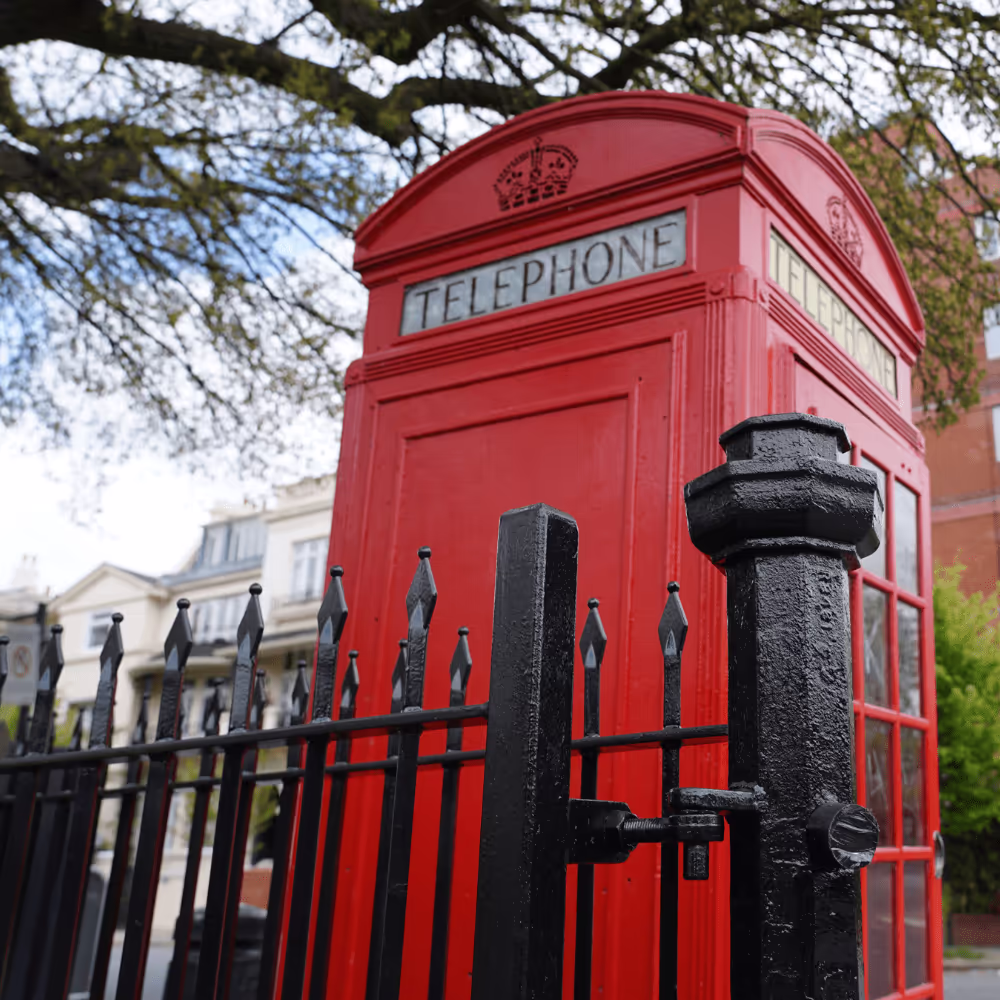 A classic red telephone box viewed through a newly refurbished heritage iron gate, demonstrating the restoration of iconic street furniture for The Royal Parks.