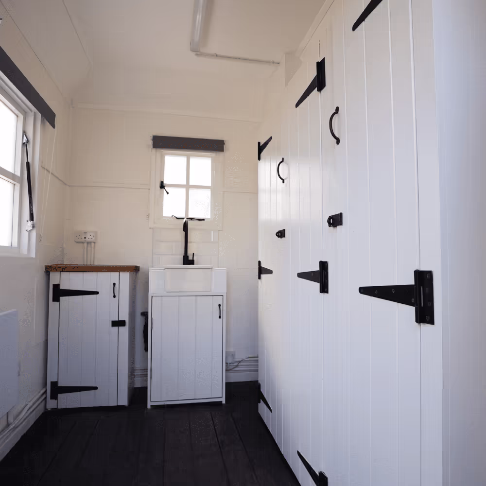 The bright, clean interior of a refurbished heritage welfare facility in a Royal Park, featuring white panelled units with traditional black ironmongery.