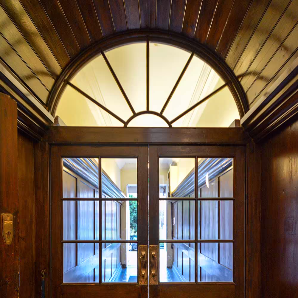 The beautifully preserved dark wood entrance lobby of a heritage building, featuring glazed double doors and an elegant arched fanlight window.