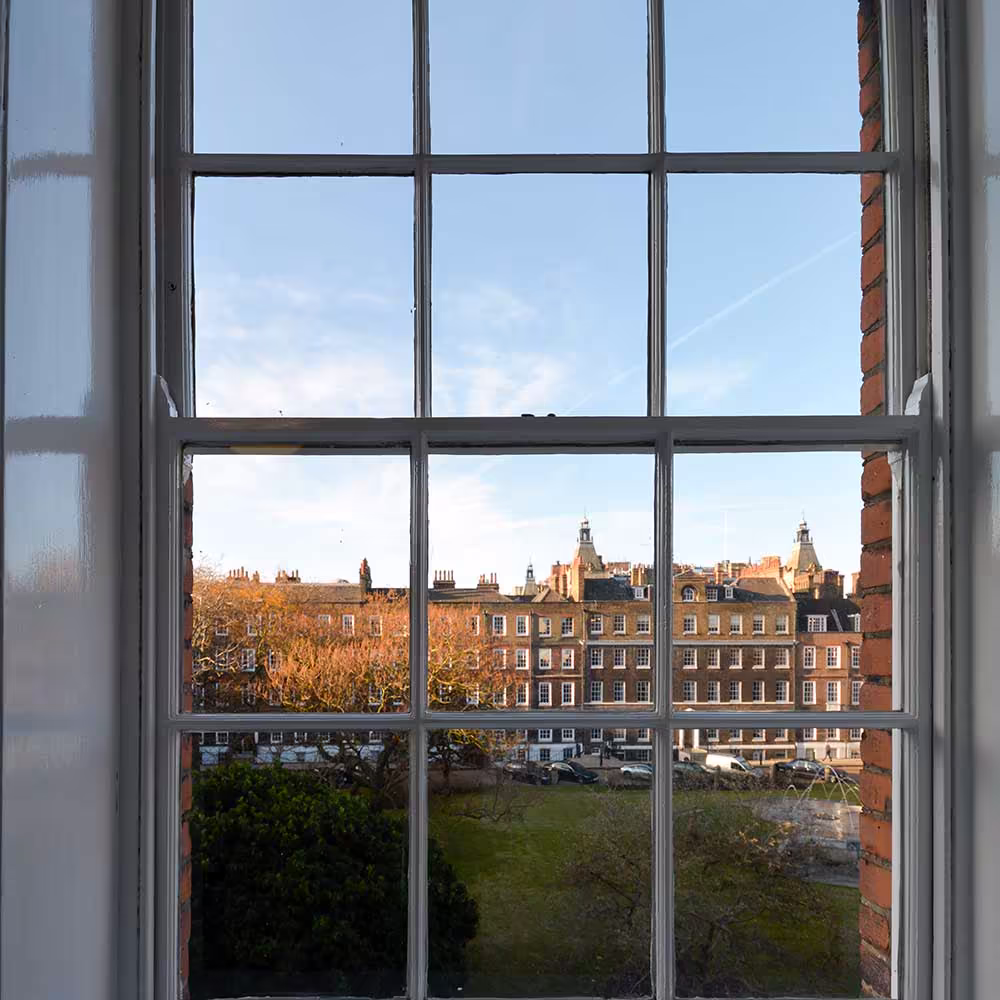 A classic view of a London square through a refurbished multi-paned sash window of a heritage property.
