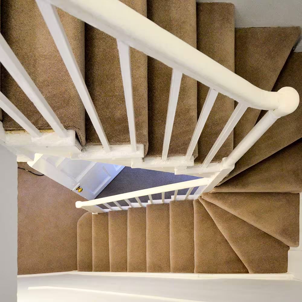 Top-down view of a newly carpeted winder staircase with a traditional white-painted spindle balustrade, part of a heritage void refurbishment.