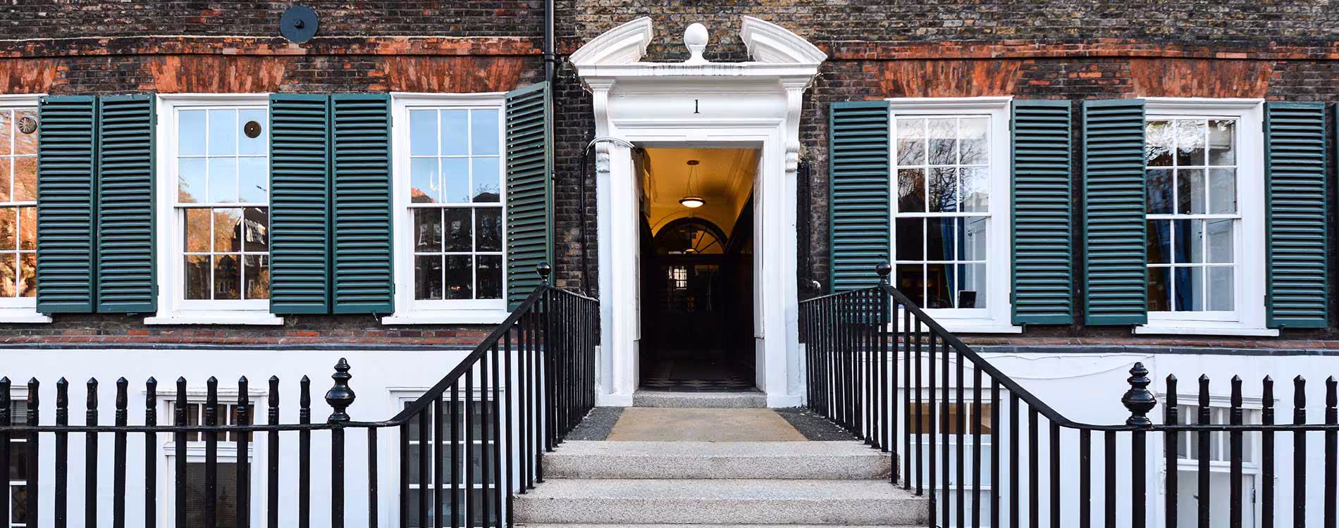 The grand entrance to a Grade II listed Georgian town house, featuring an ornate white pedimented doorway and sash windows with traditional green shutters.