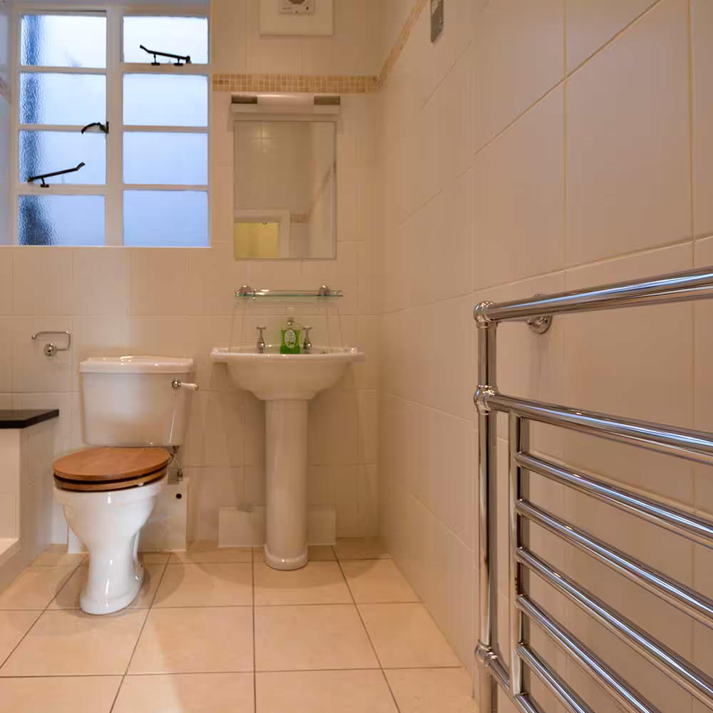 A classic bathroom from the high-end refurbishment project, featuring a traditional toilet with a wooden seat, a pedestal sink, and a large chrome heated towel rail.