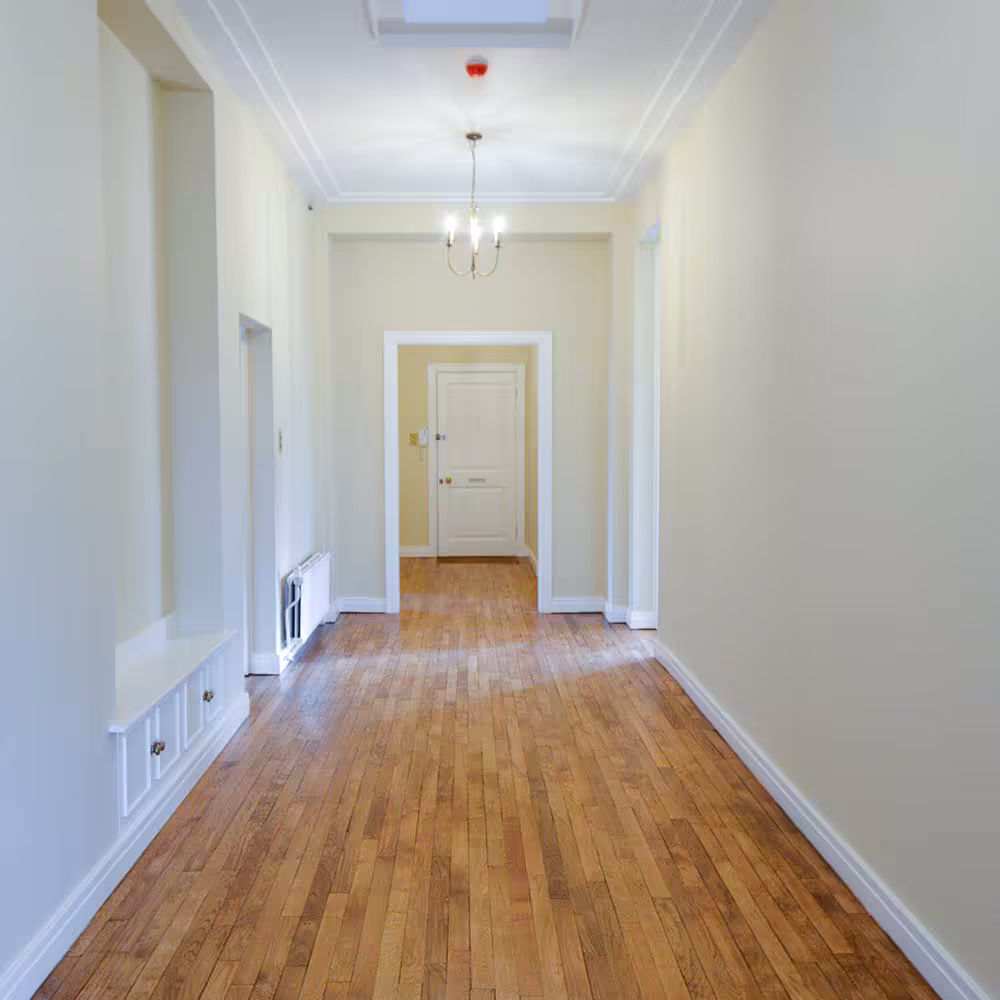 A grand, spacious hallway after a high-end refurbishment, showing the beautifully restored polished hardwood floors and high ceilings.