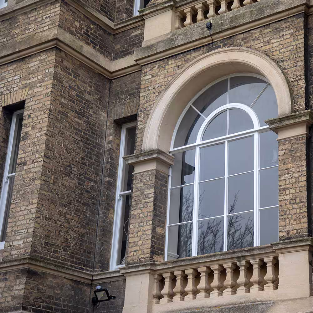 A close-up of a large, repaired arched window on a historic building, showcasing the restored stone arch and balustrade against the old brickwork.