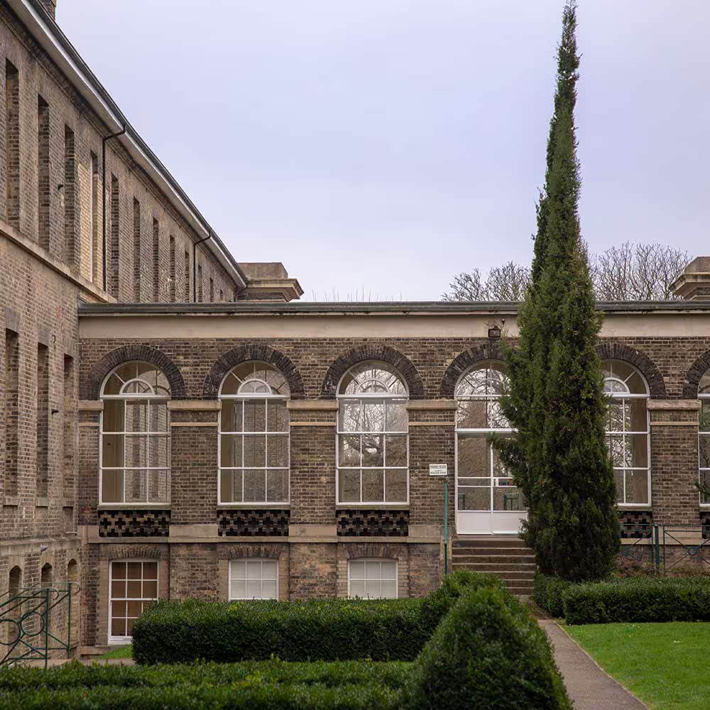 The courtyard of a historic building after repairs, featuring a row of large, restored arched windows set into the brick facade, with a manicured garden in the foreground.