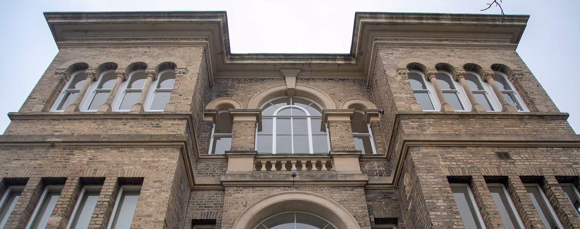 A low-angle view looking up at the grand, symmetrical facade of a historic brick building after extensive repairs and restoration of its windows and stonework.