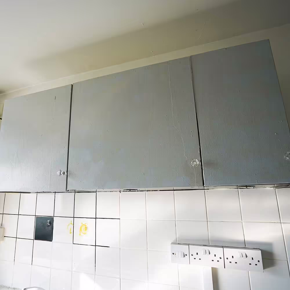 Close-up of old, poorly maintained kitchen cabinets and stained wall tiles, highlighting the need for replacement in a council property.