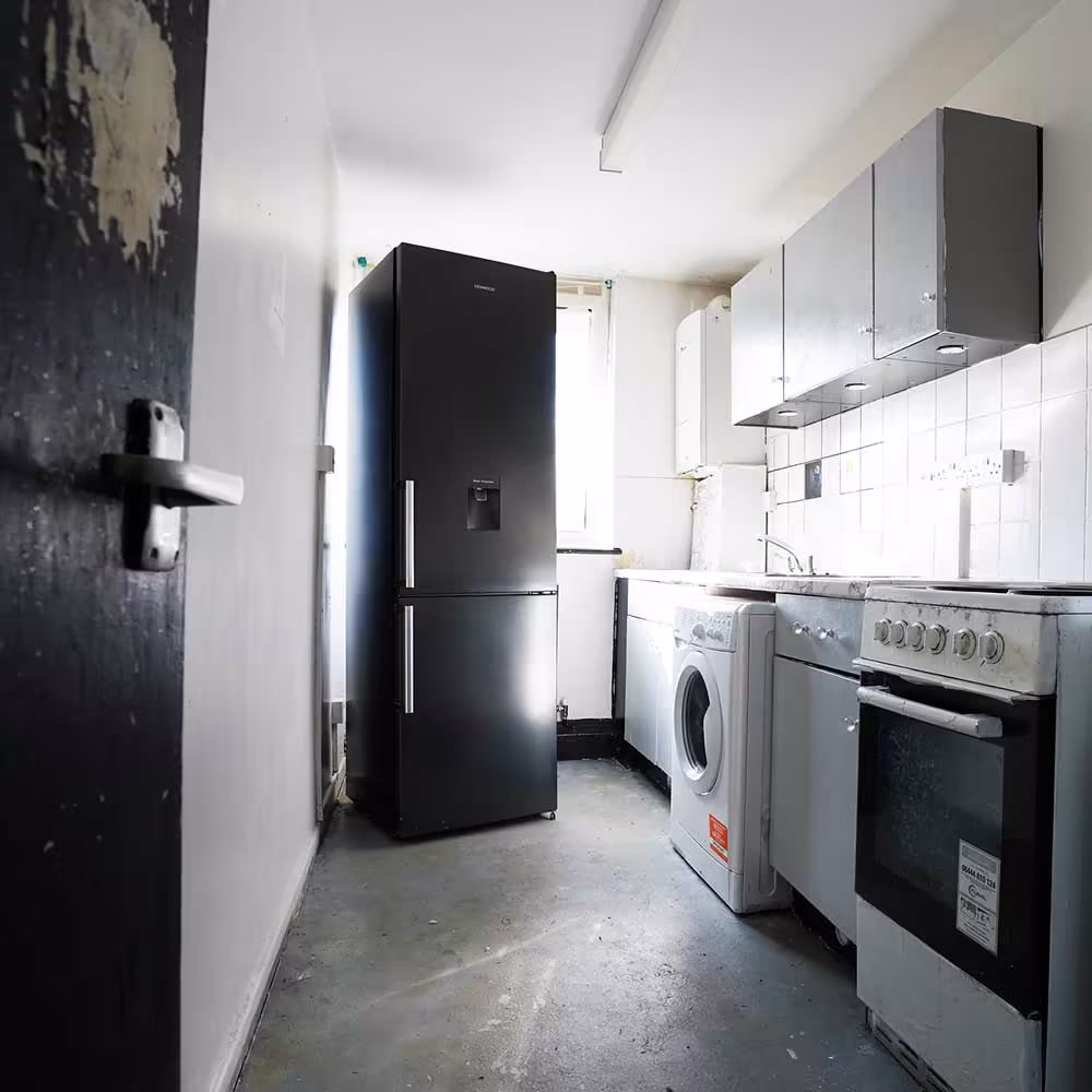 A dated galley kitchen in a Westminster City Council property before its scheduled replacement, showing old appliances and worn flooring.