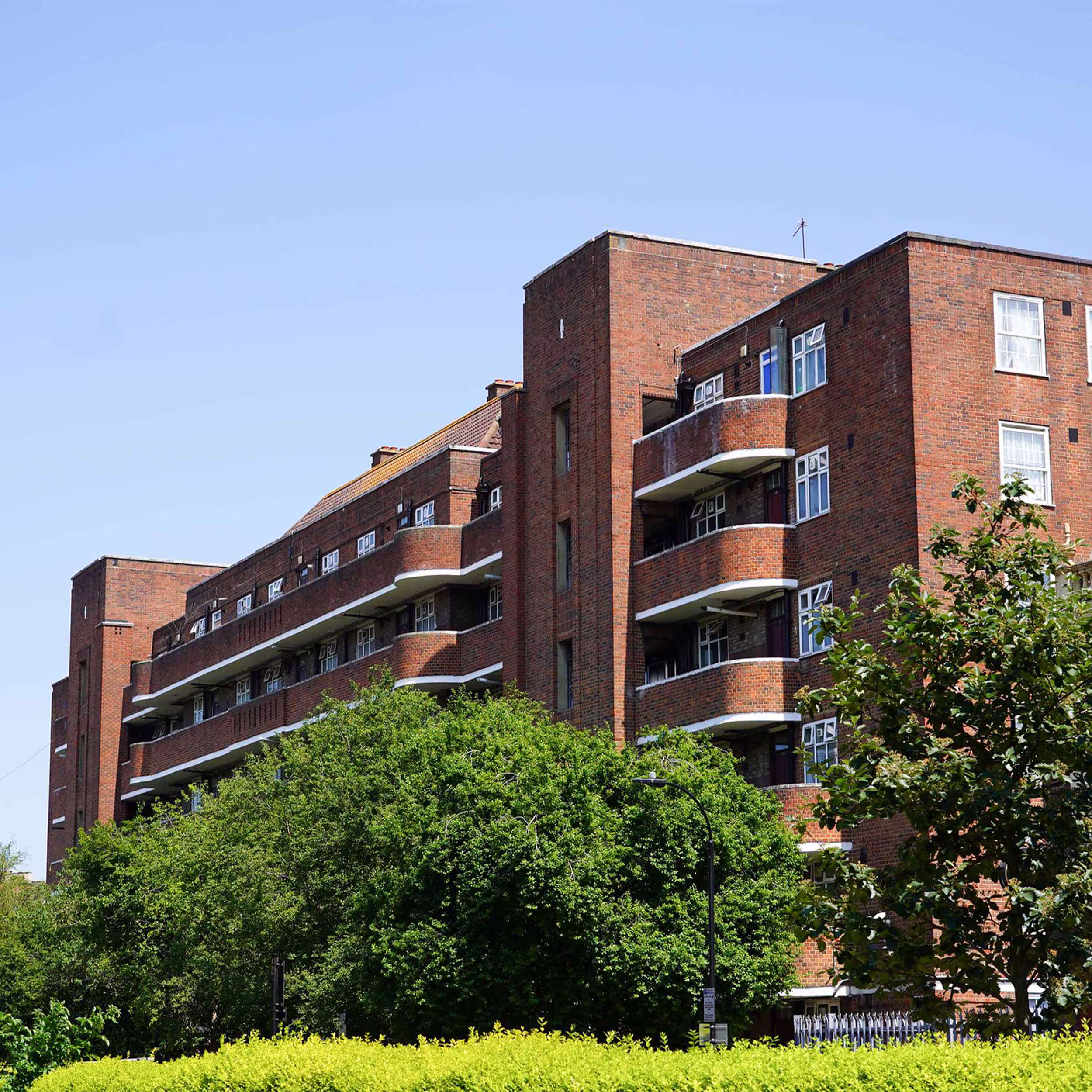 The exterior of a classic 1930s-style red brick apartment block on the estate, featuring distinctive curved balconies, which is part of the major refurbishment works.
