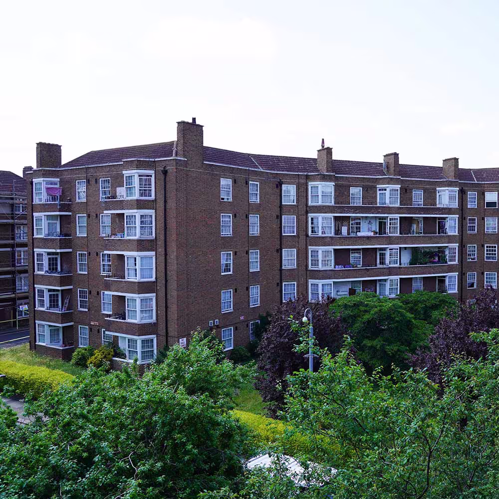 An elevated view of a large, curved brick residential block on the estate, surrounded by mature trees, showcasing the scale of the major refurbishment project.