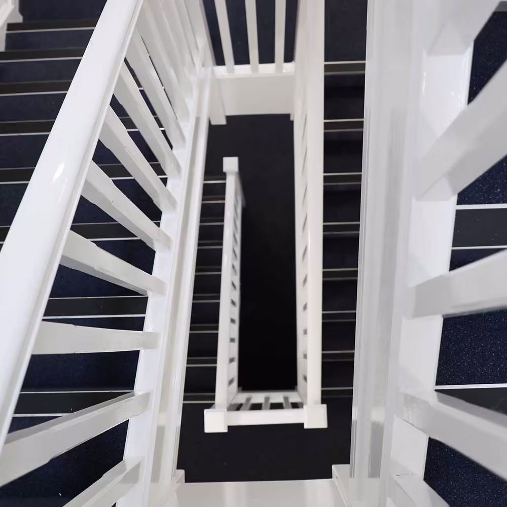 Top-down view of a newly refurbished multi-flight staircase, showing the clean white balustrades and dark carpet creating a geometric pattern.