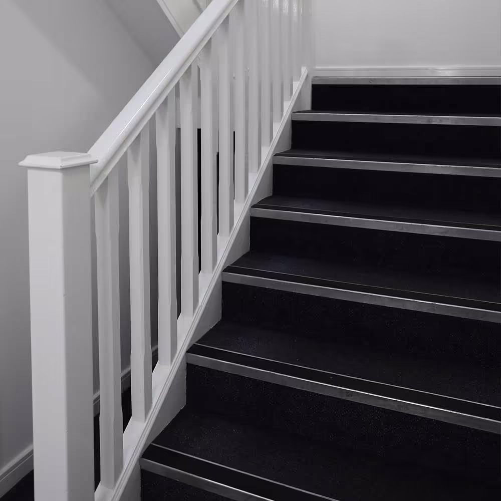 A freshly repaired and painted communal staircase with a white balustrade and new dark carpet treads with safety nosings.