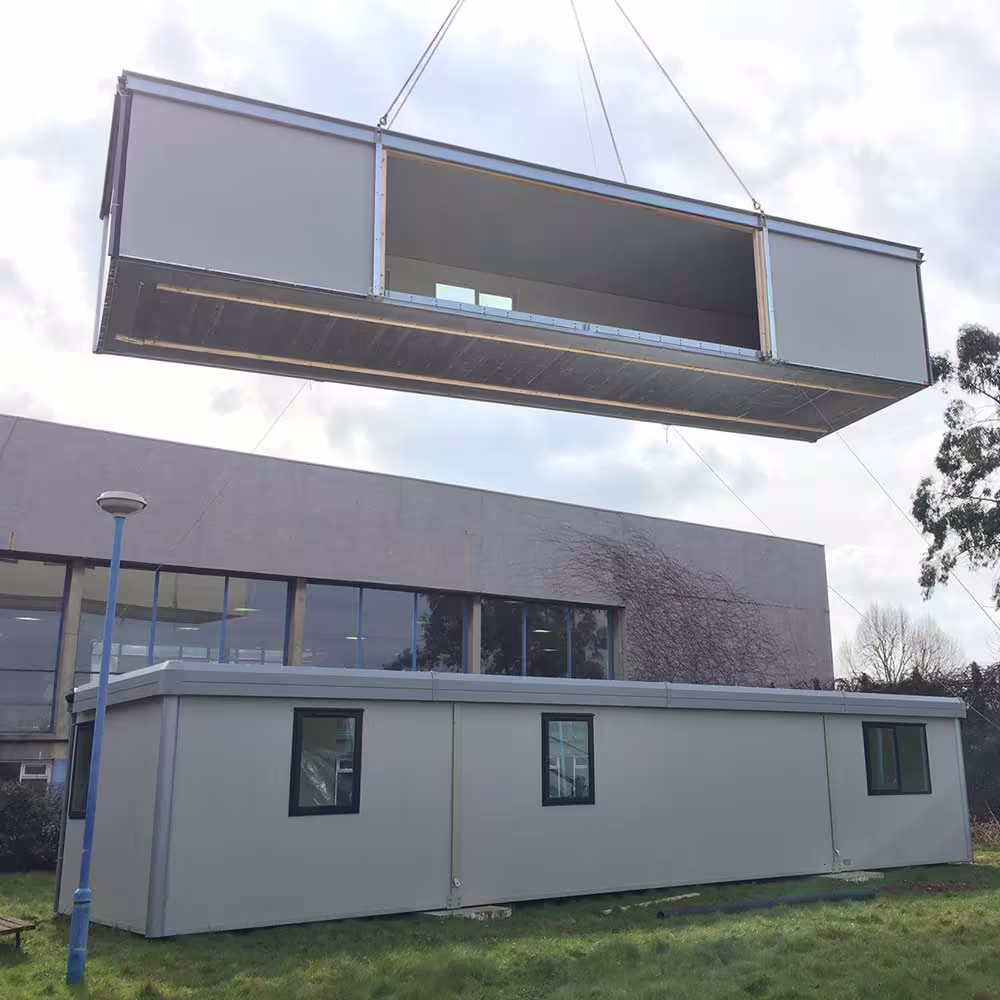 Crane positioning a prefabricated module onto the foundation at a modular construction site.