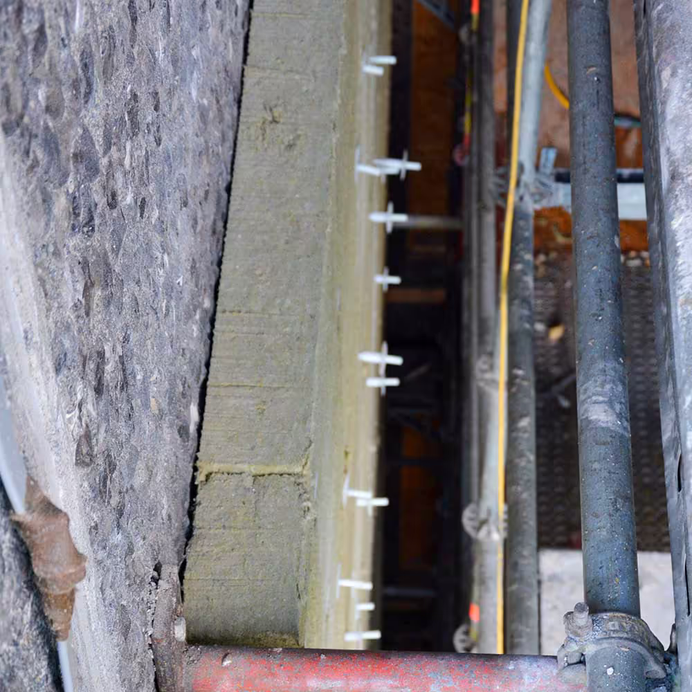A detail shot showing the thickness of the external wall insulation and the mechanical fixings used to secure it to the building's facade during planned improvements.