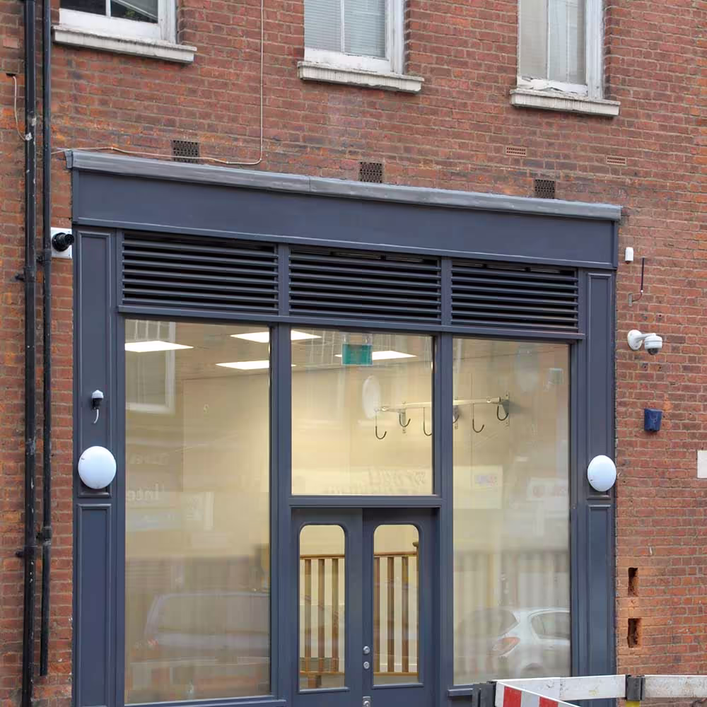 The newly installed and modernised grey shopfront of the police building, featuring large windows and integrated ventilation louvres, set into a traditional red brick facade.