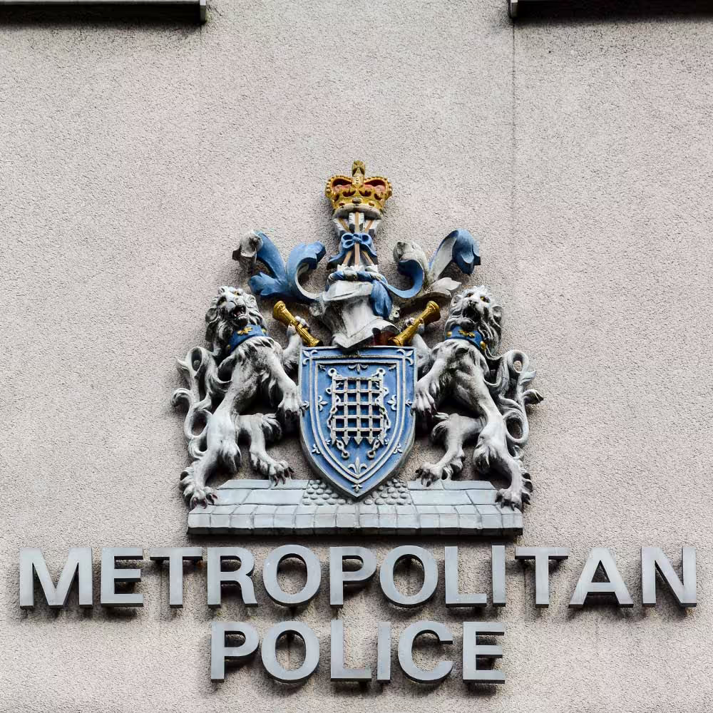 The official crest and title of the 'Metropolitan Police' mounted on the exterior wall of a station, showing the detailed coat of arms.