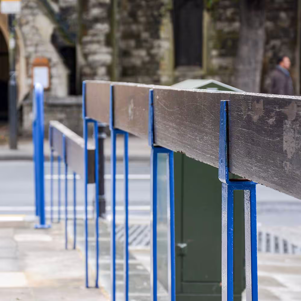 A close-up of a repaired and repainted blue metal barrier with a wooden top rail, part of the external repair works for a police station.