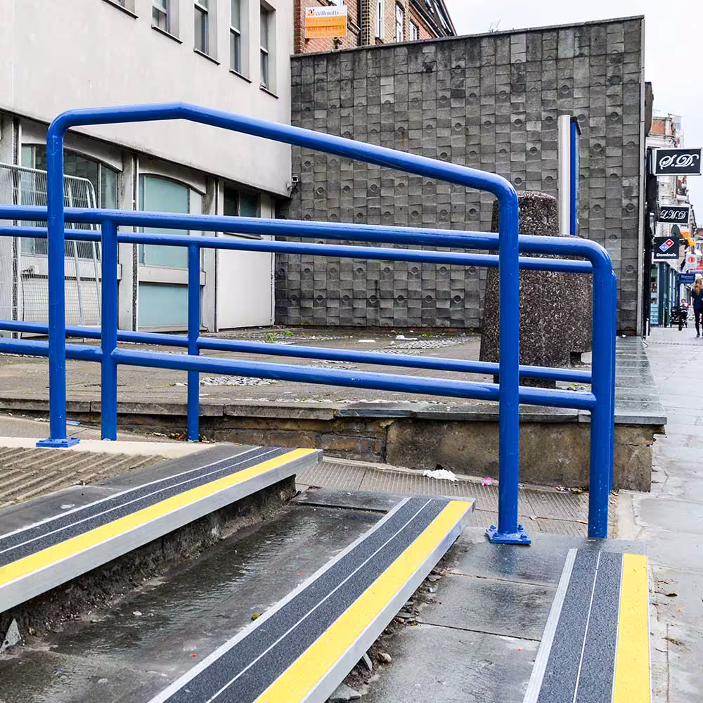 Newly installed external access steps at a police station, featuring bright blue safety handrails and high-visibility yellow and black anti-slip treads for public safety.
