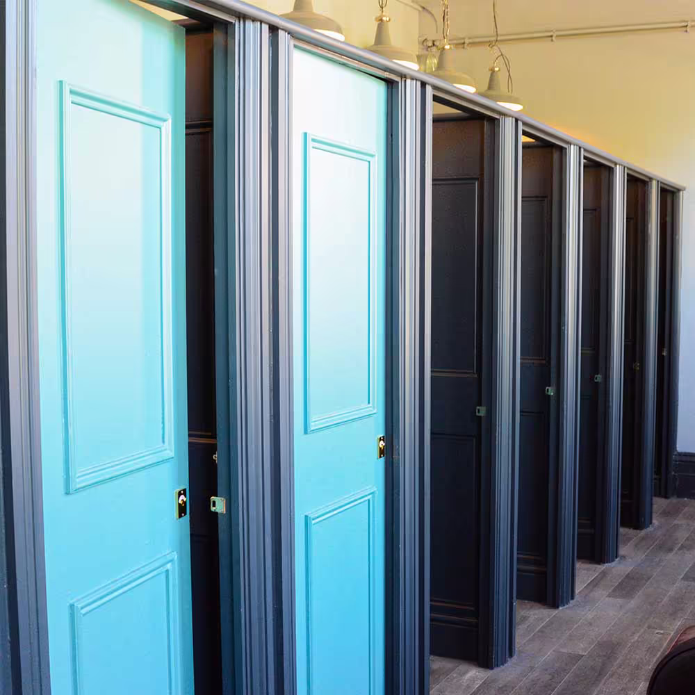 A row of newly refurbished toilet cubicles in the pub, featuring a stylish design of alternating bright turquoise and dark grey panelled doors.