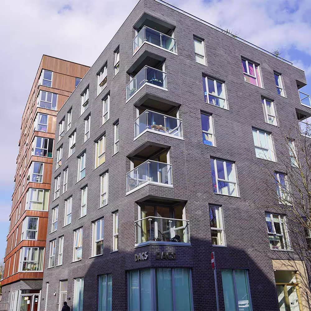 The corner of the dark grey brick apartment block, named DACS, with the taller copper-cladded building visible behind, showcasing the different finishes in the re-cladding project.