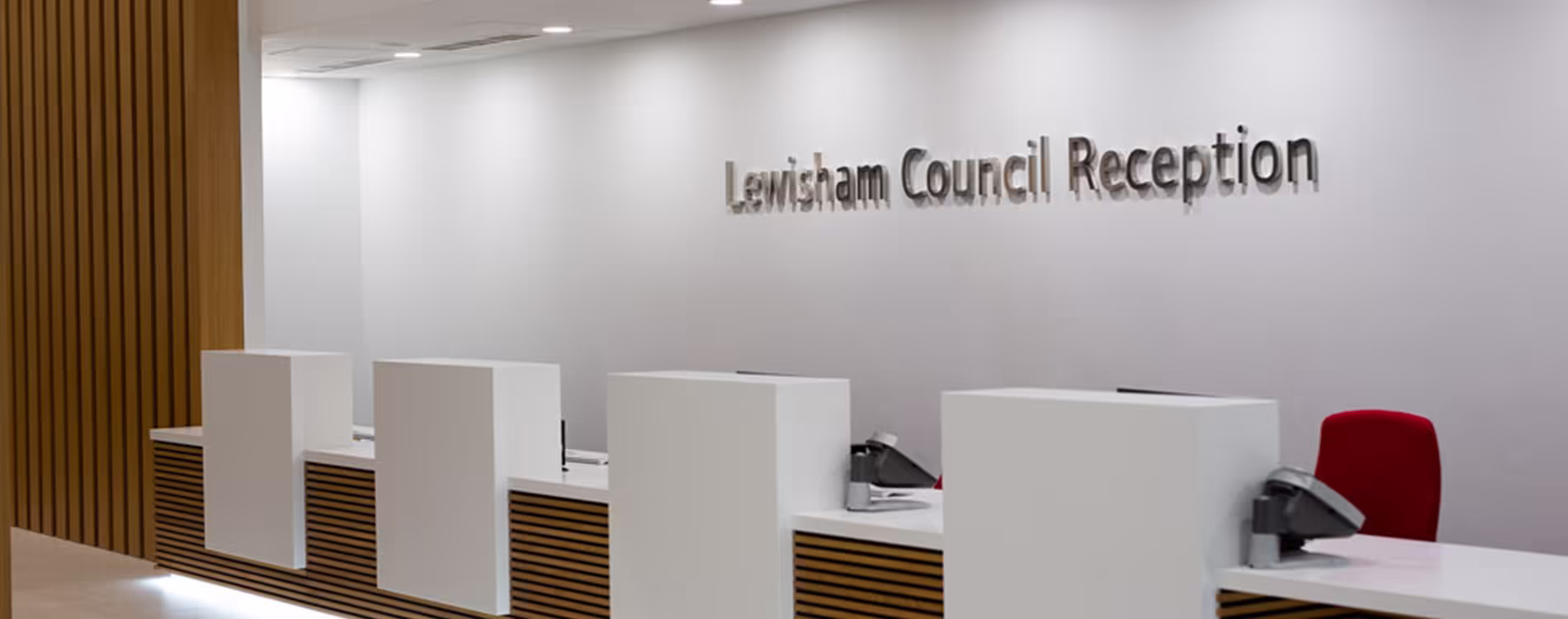 The newly refurbished Lewisham Council Reception, featuring a modern, long counter with individual white privacy pods, wood-slat detailing, and 3D lettering on the wall.