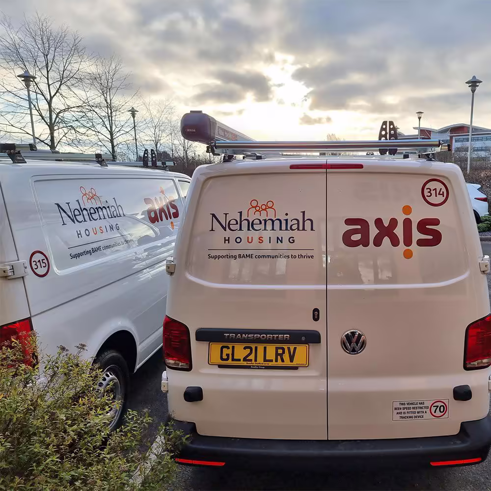 The back of two white service vans parked side-by-side, both featuring the co-branded logos of Axis and Nehemiah Housing for their repair service contract.