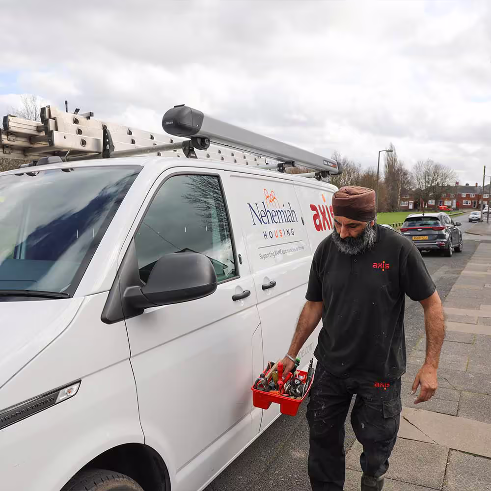 An Axis operative carries his toolbox from his co-branded Nehemiah Housing van, walking along a pavement to carry out a repair for a resident.