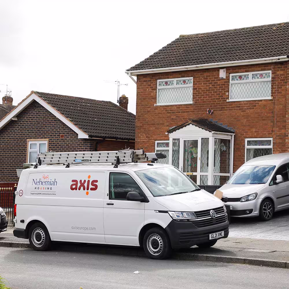 An Axis and Nehemiah Housing co-branded service van parked on a residential street in front of a house, ready to provide repair services to tenants.
