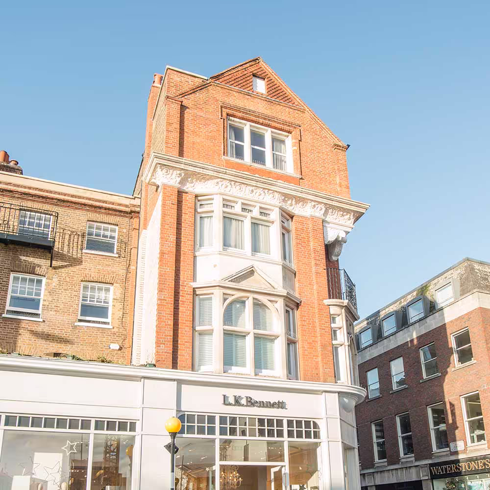 An upward view of the historic building's facade after repair, focusing on the central gable and bay window structure above the L.K. Bennett store against a bright blue sky.