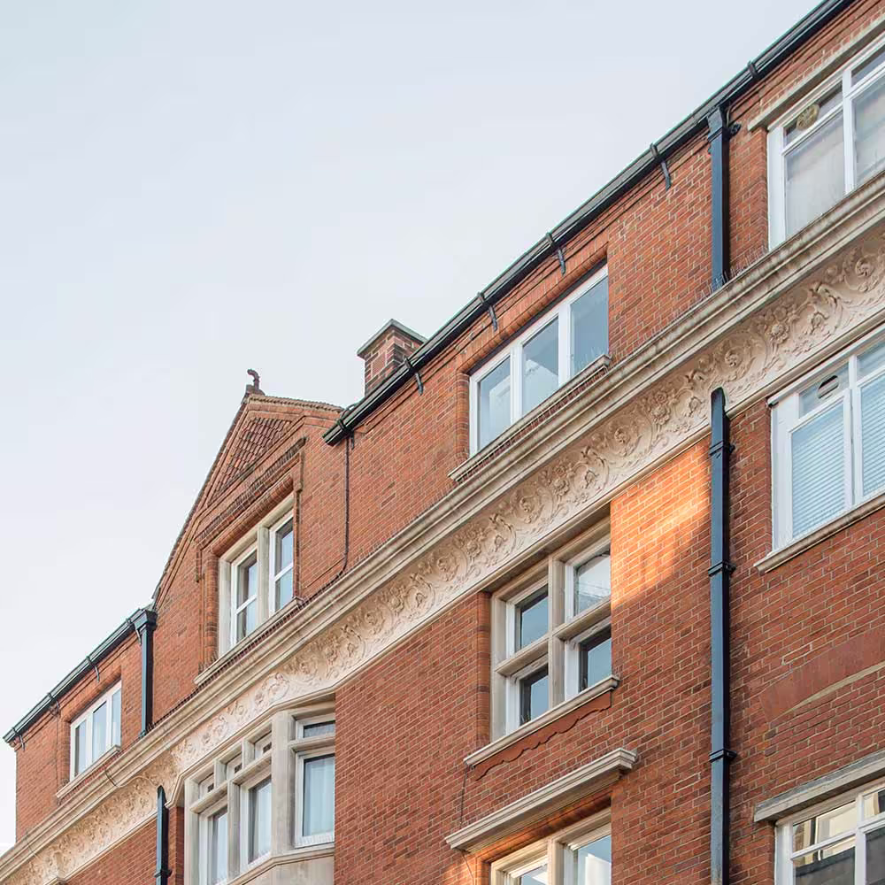 A detailed shot of the building's facade after redecoration, showing the intricate, restored white carved stone frieze running below the top-floor windows.