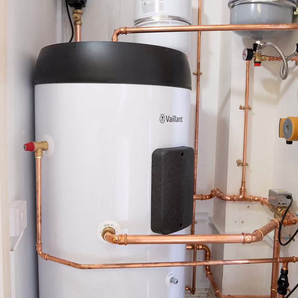The indoor components of a residential ASHP system, featuring a large white Vaillant hot water cylinder and expertly fitted copper pipework in a utility cupboard.