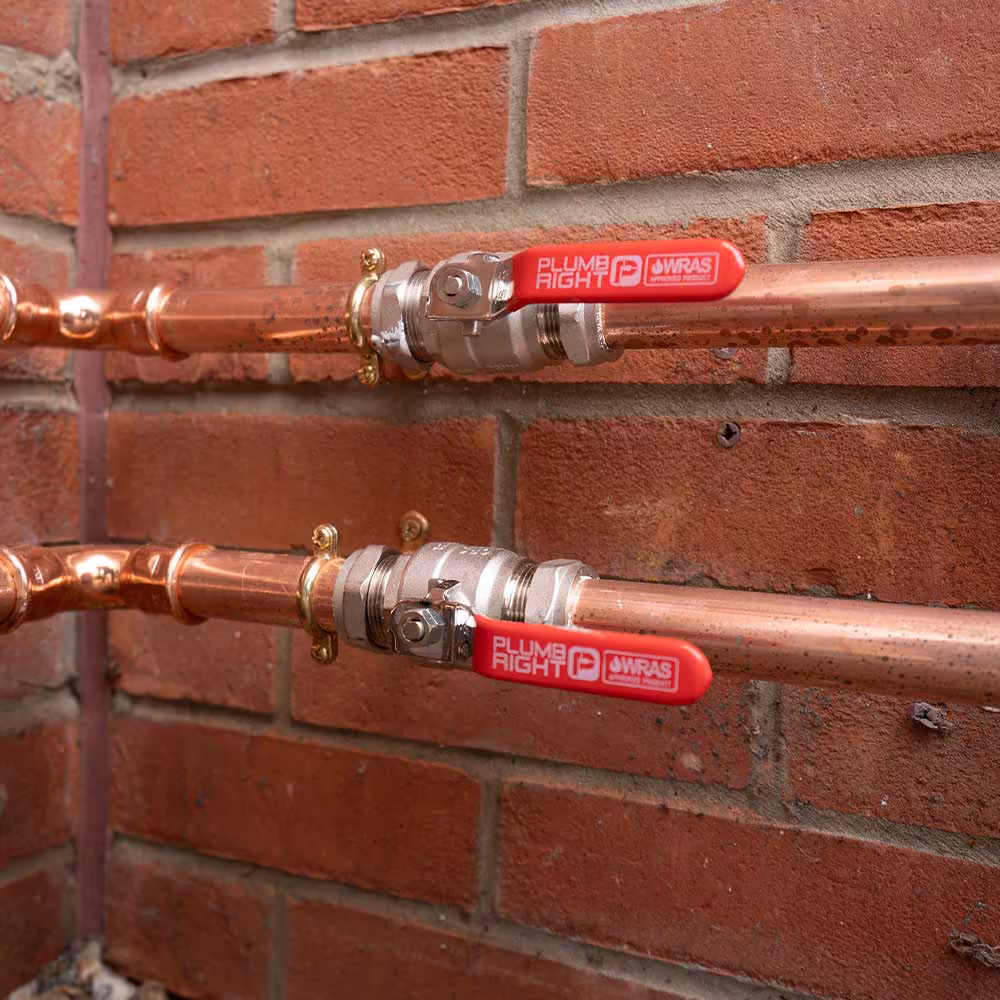 A close-up of the neat external pipework for an ASHP installation, showing two copper pipes with red-handled WRAS approved valves fixed to a brick wall.
